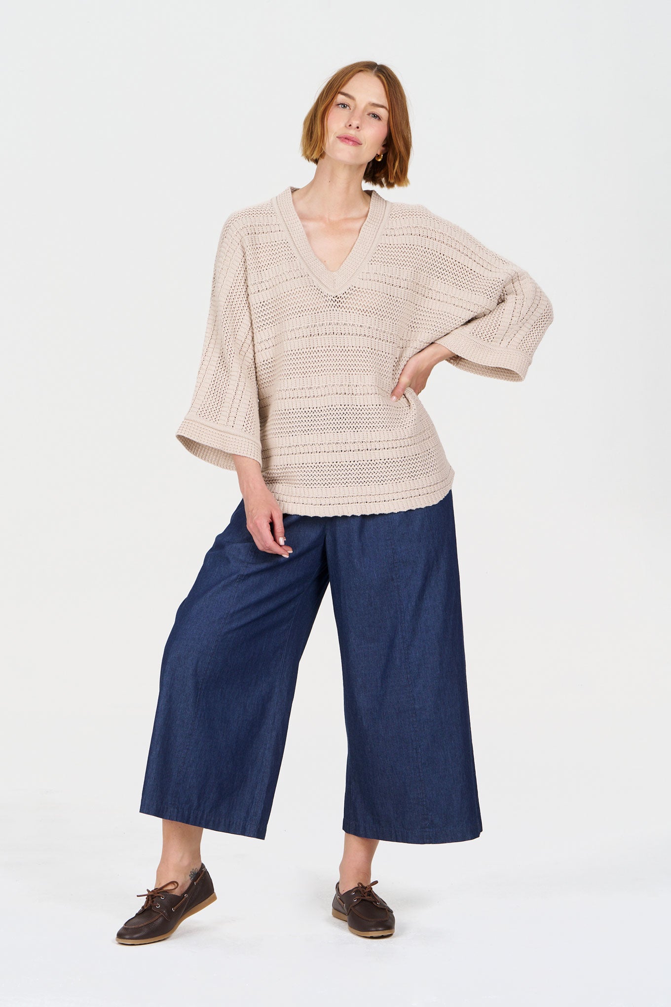 Model wearing a cozy beige crochet knit sweater paired with wide-leg blue denim pants.