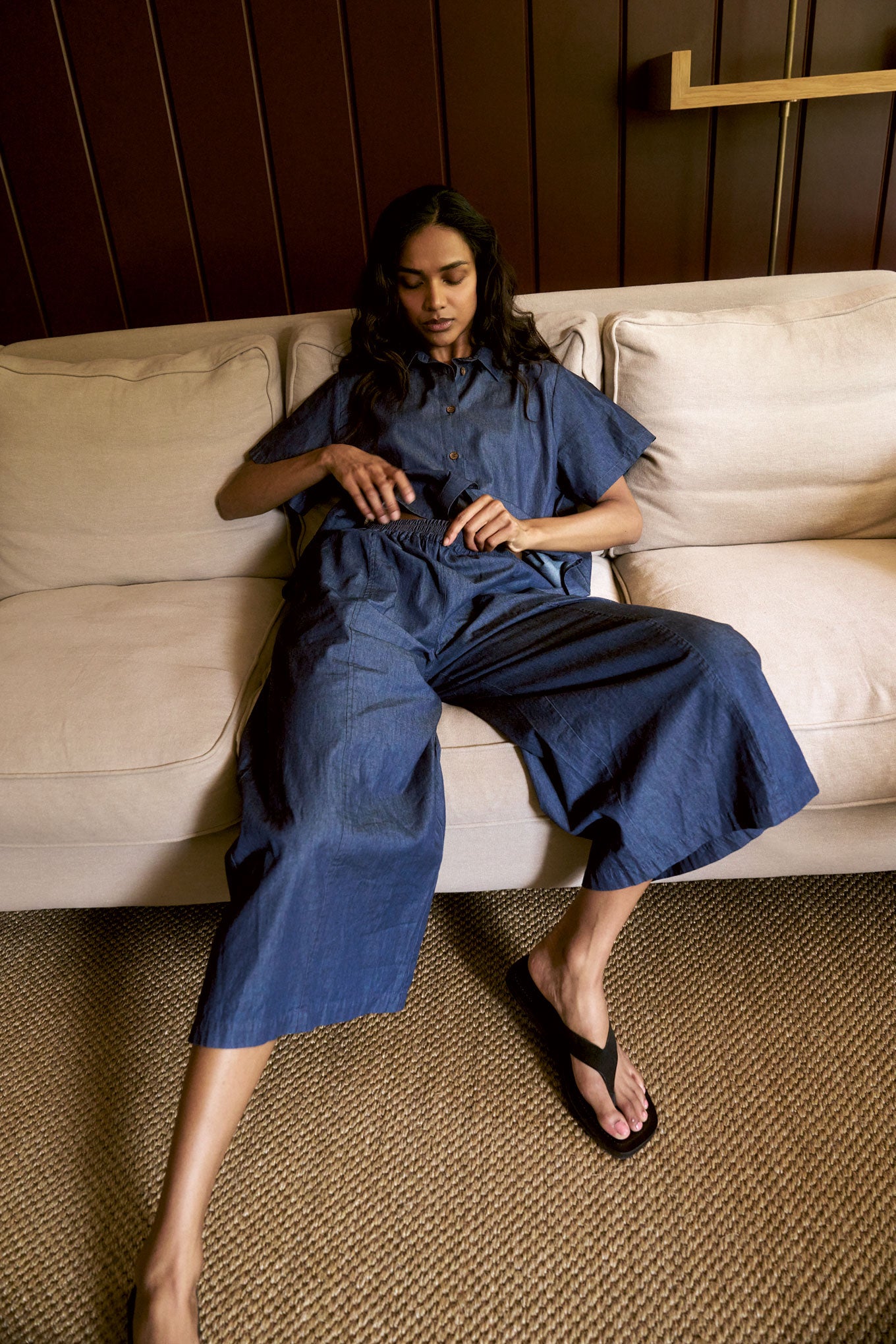 Model wearing DANI Organic Cotton Coulotte - midwash, sitting on a sofa, relaxing in a stylish outfit.