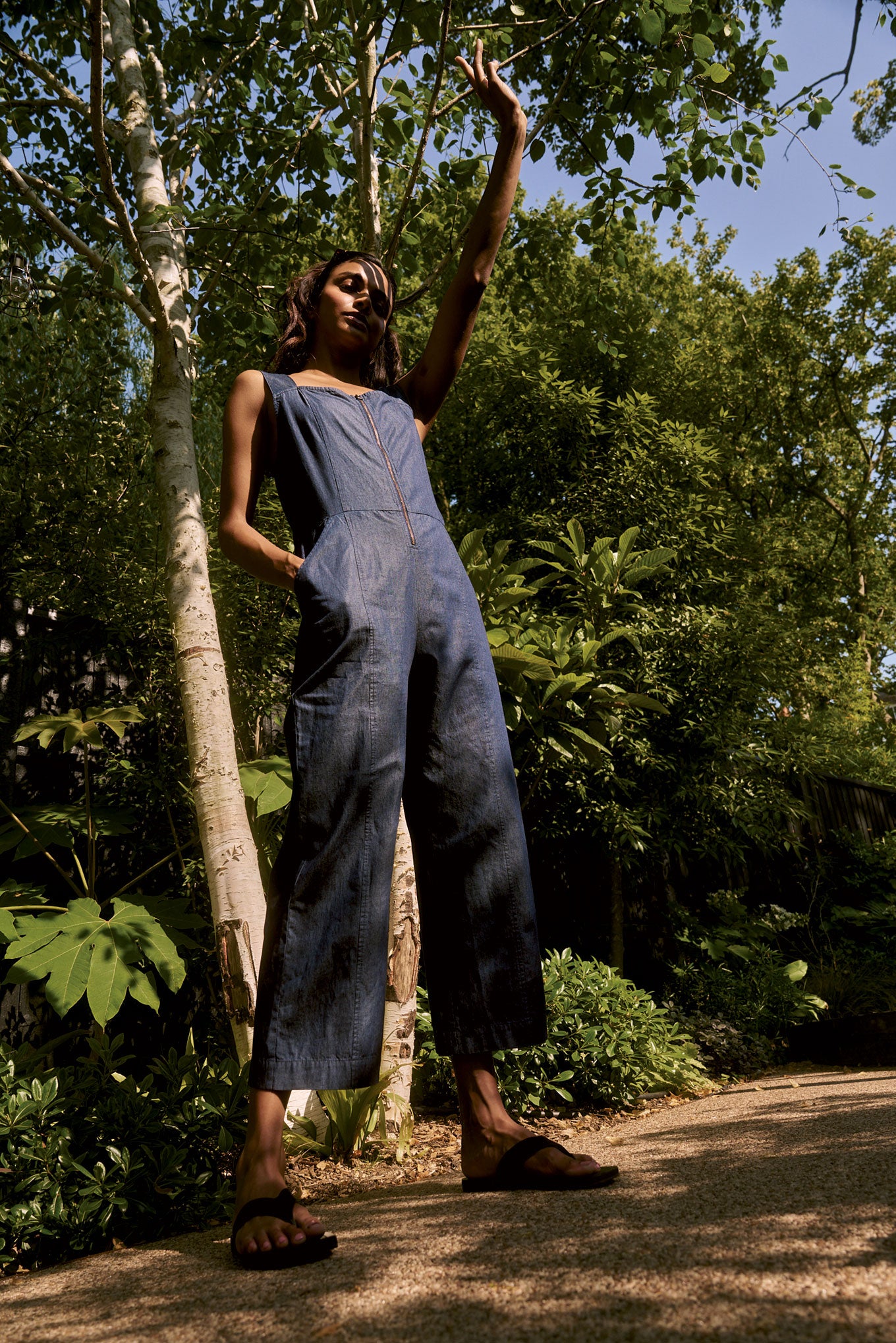Model wearing DAY Organic Cotton Jumpsuit - midwash against a lush green backdrop.