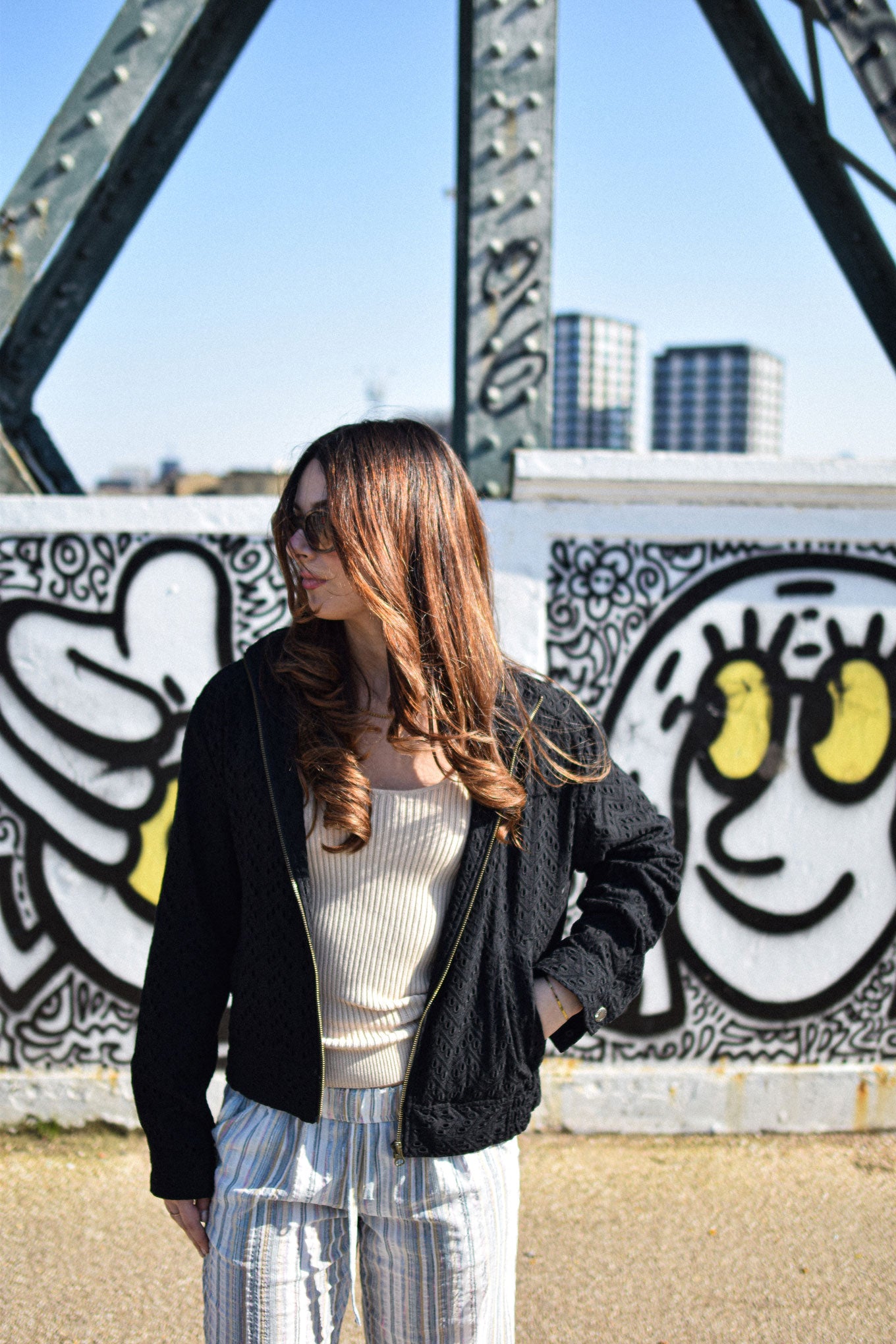 Woman wearing LOTUS Organic Cotton Jacket - Black outdoors, with graffiti background.