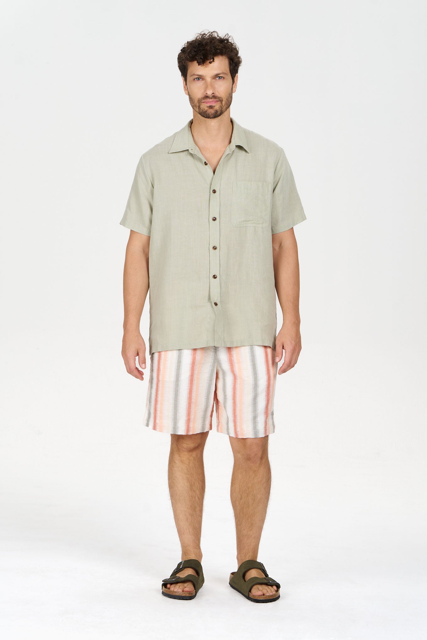 Man wearing LOYLE Tencel Linen Shirt - Sage with striped shorts and sandals.