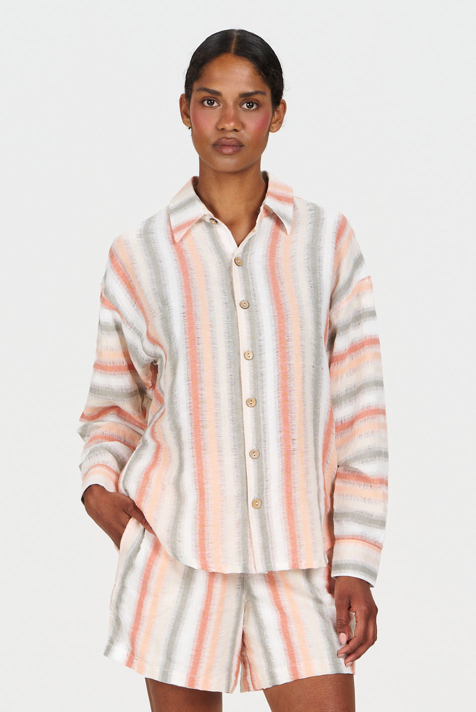 Model wearing SUNSET Organic Cotton Shirt - Stripe featuring soft pastel colors and buttons, paired with matching shorts.