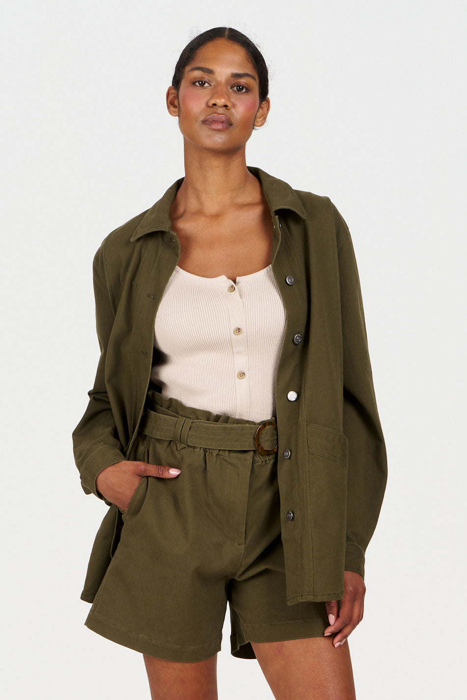 COVE Vest Organic Cotton Vest - Sand worn with an olive green jacket and shorts, showcasing a stylish casual outfit.