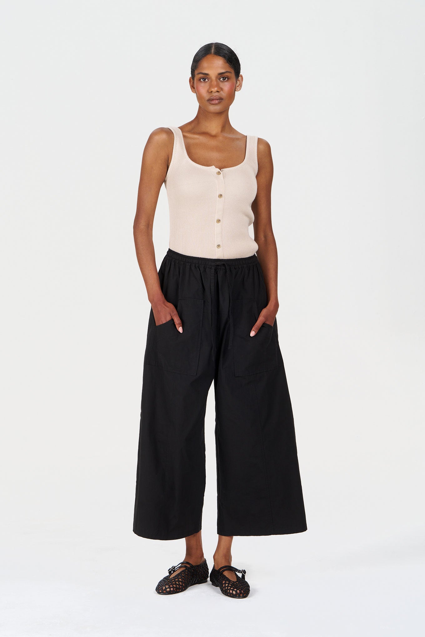 Model wearing COVE Vest Organic Cotton Vest - Sand with wide-leg black pants and sandals.