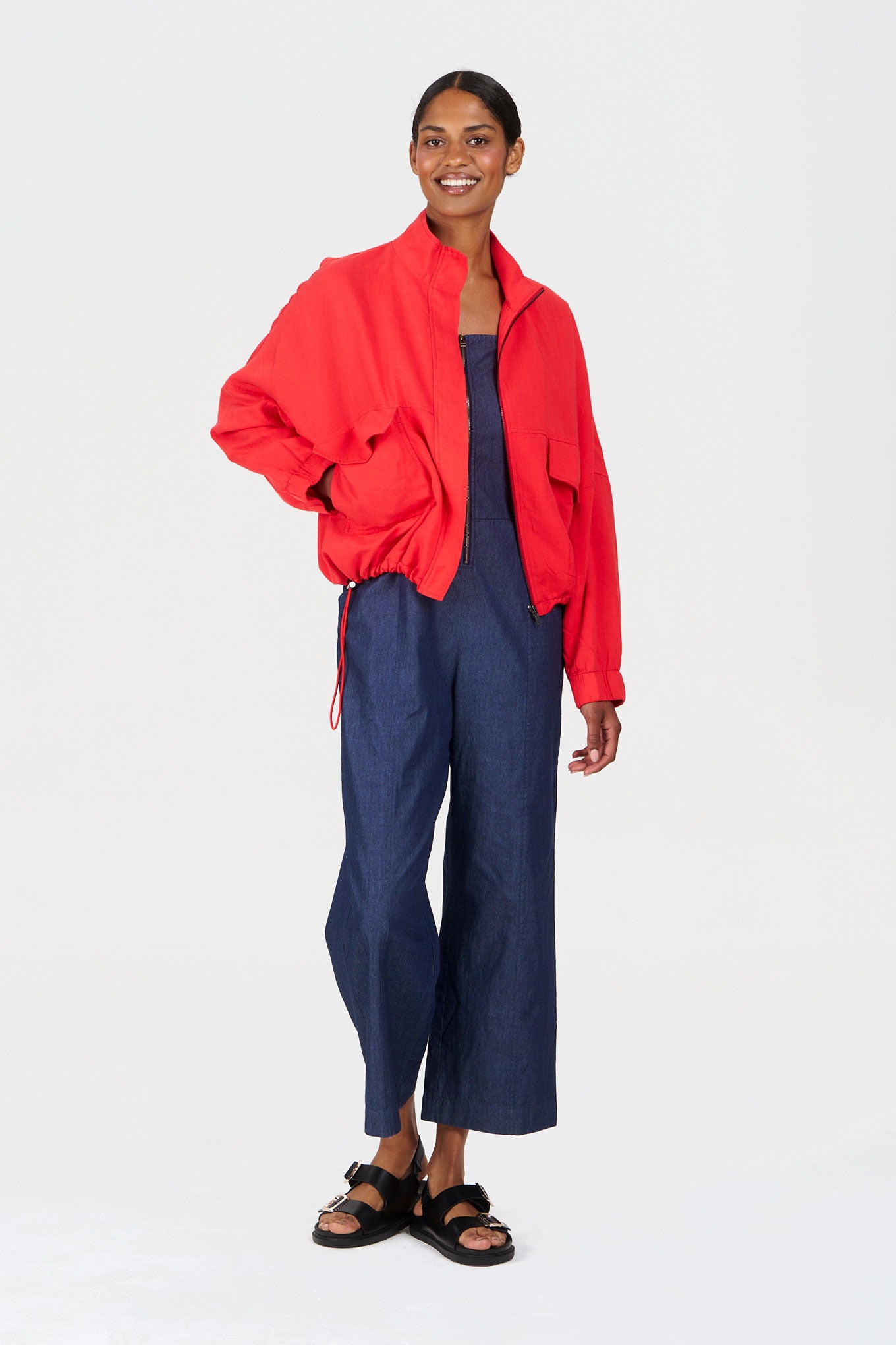 DAY Organic Cotton Jumpsuit - midwash worn with a red jacket, model standing confidently in stylish outfit.