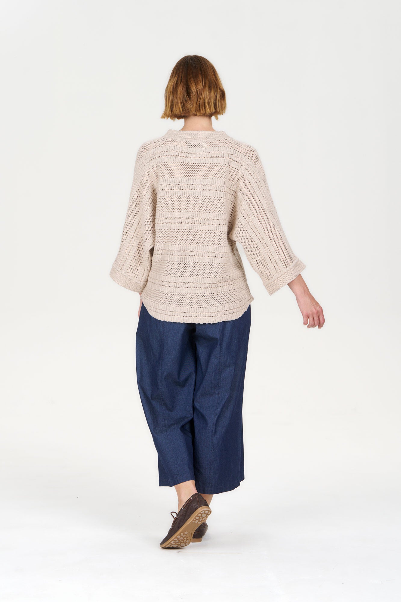 Back view of a model wearing the COLADA Organic Cotton Tee - Sand with blue pants and casual shoes.
