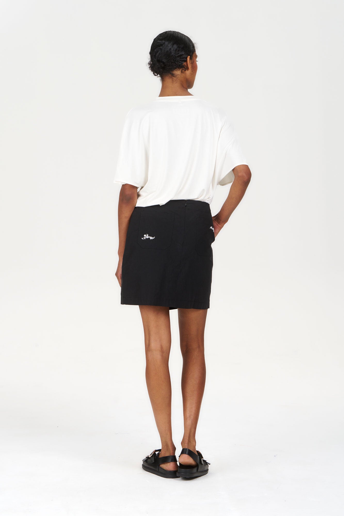 Model wearing the WILLOW Organic Cotton Skirt - Black with a white top and sandals, showcasing a stylish back view.