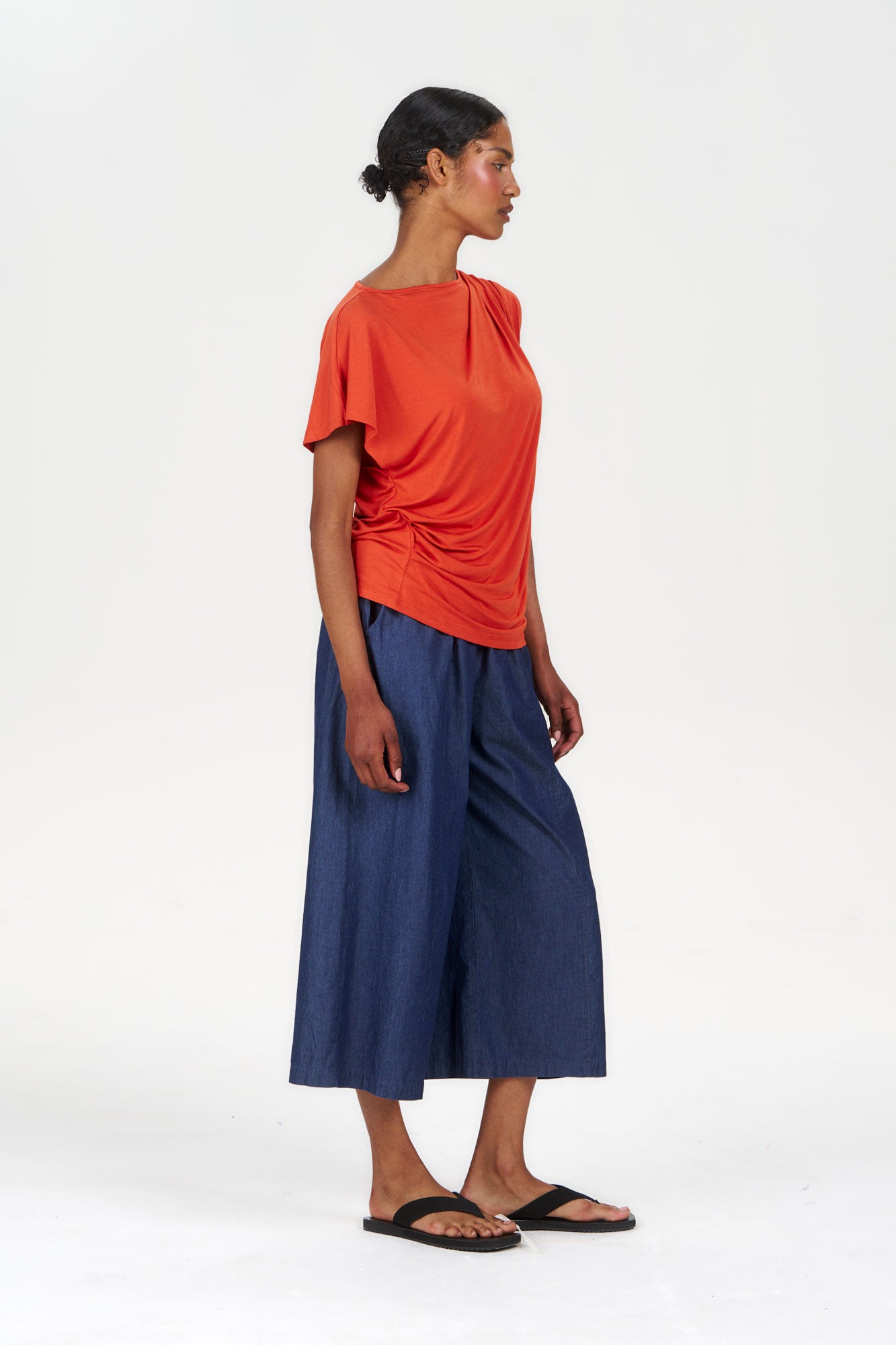 CATE Modal Top - Orange worn with wide blue culottes and sandals, showcasing a stylish side profile.