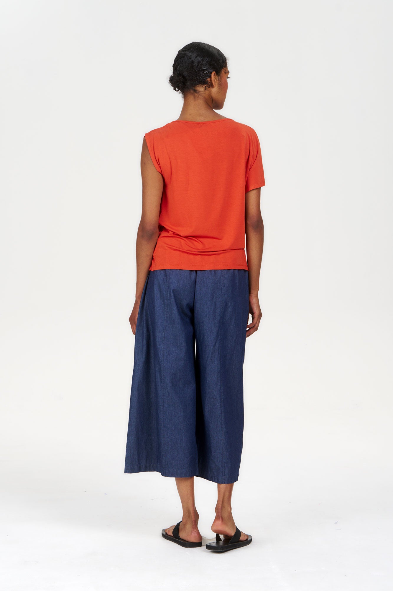 Back view of a model wearing the CATE Modal Top - Orange paired with wide-leg navy pants.