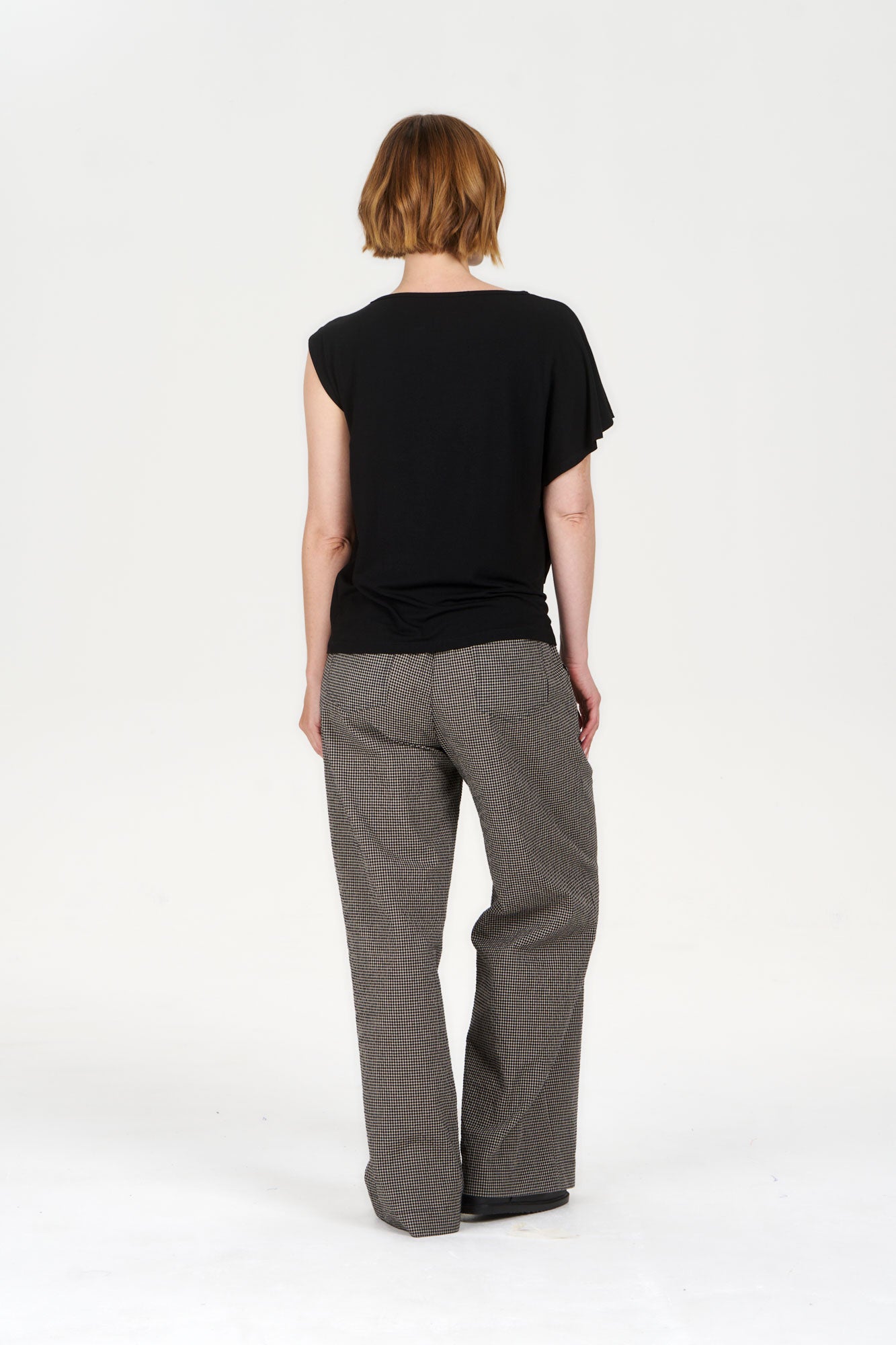 Model wearing CATE Modal Top - Black with loose pants, showcasing the back view in a minimalistic setting.