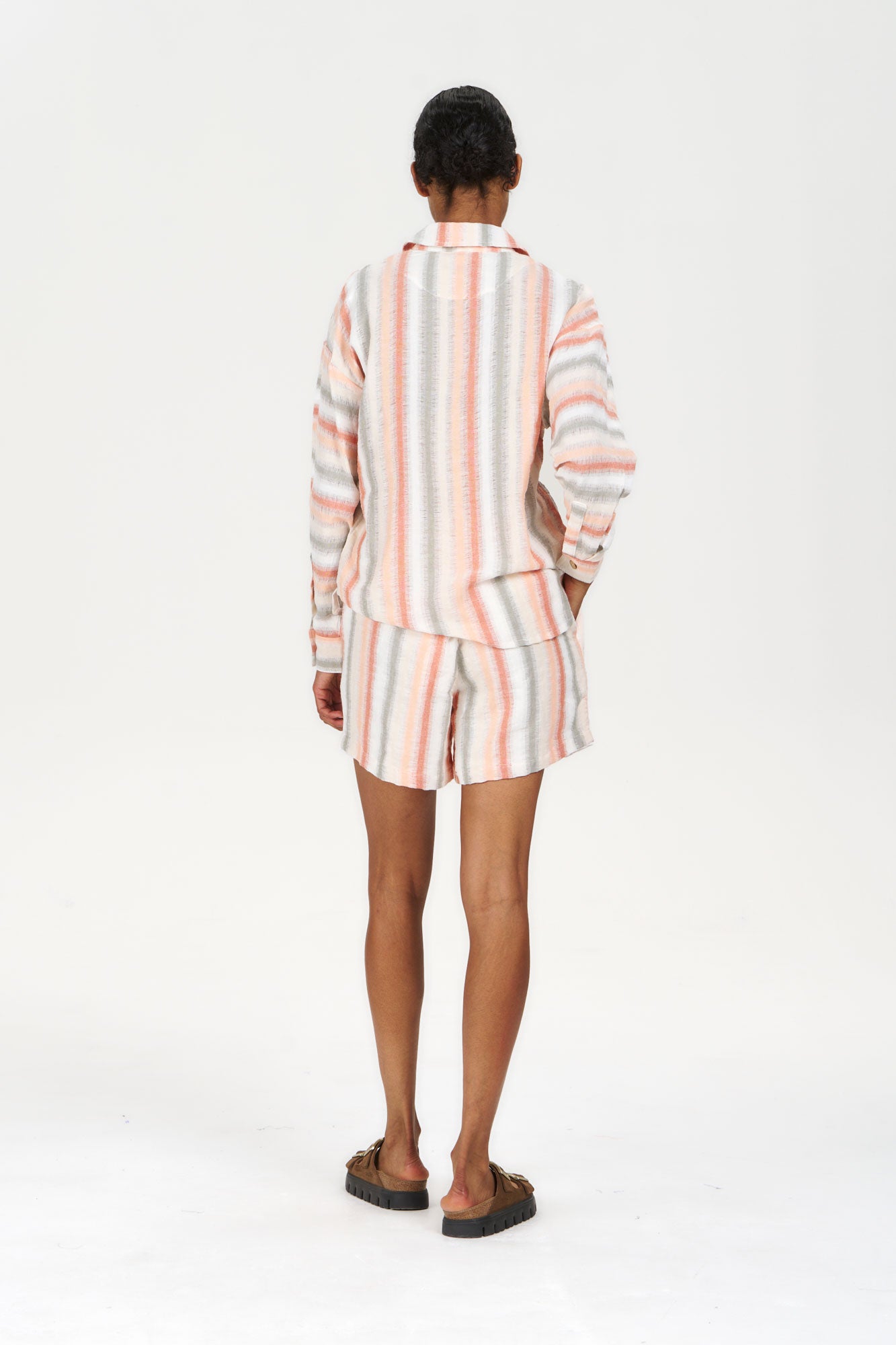 Back view of a model wearing the SUNSET Organic Cotton Shirt - Stripe with matching bottoms, showcasing its colorful striped design.