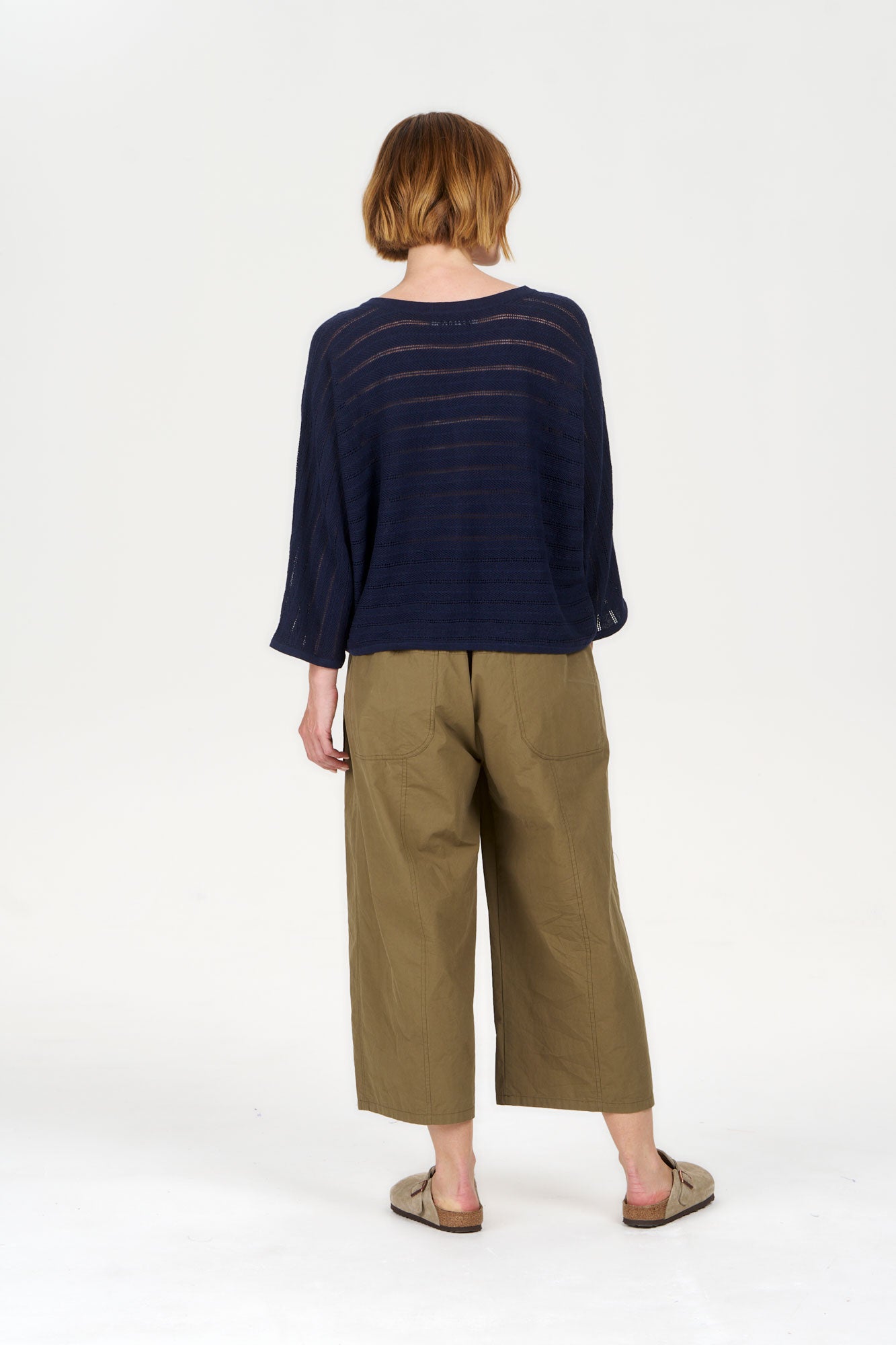 Woman wearing CLEO Organic Cotton Trouser - Khaki, seen from the back with a navy top, showcasing eco-friendly fashion.