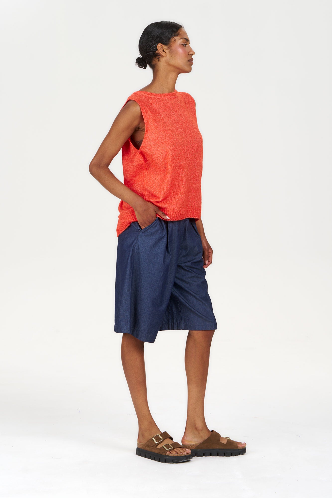 BLAKE Recycled Poly Vest - Orange worn by a model with navy shorts and sandals in a studio setting.