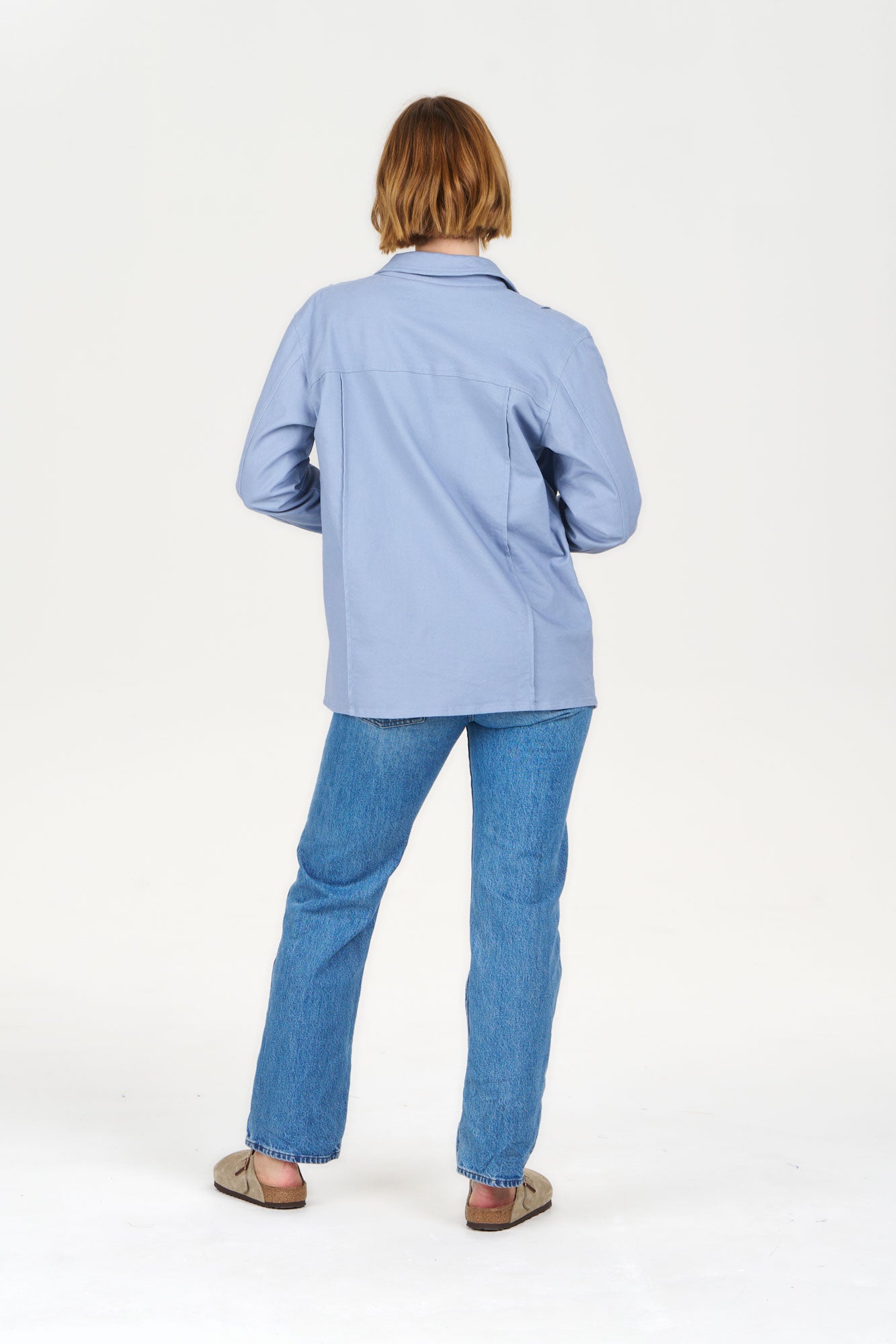 Back view of model wearing CHORE Organic Cotton Jacket - Blue with blue jeans and sandals.