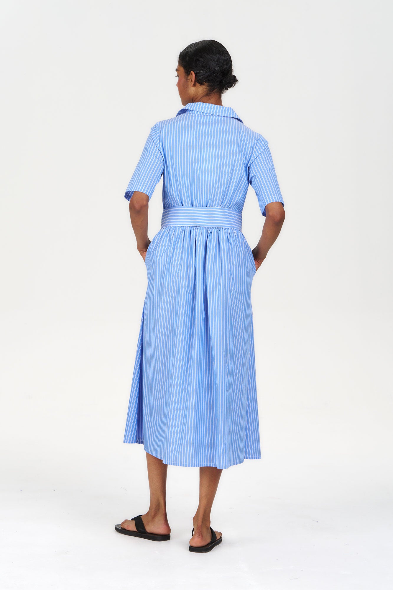 Back view of a model wearing SHORE Organic Cotton Dress - Blue Stripe, showcasing the striped design and belt detail.
