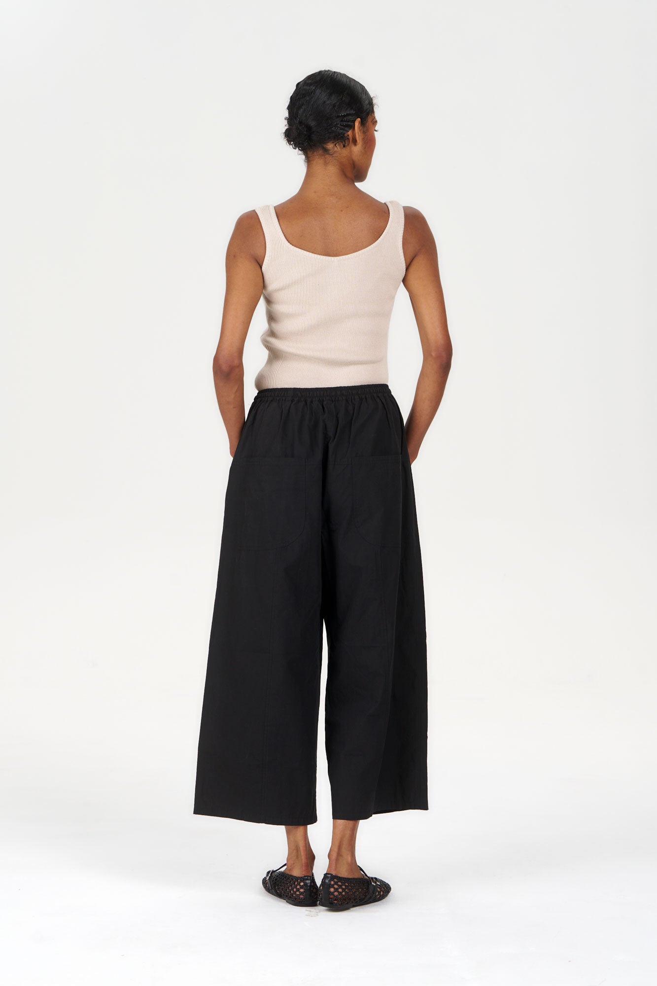 COVE Vest Organic Cotton Vest - Sand worn with black wide-leg pants from a back view.