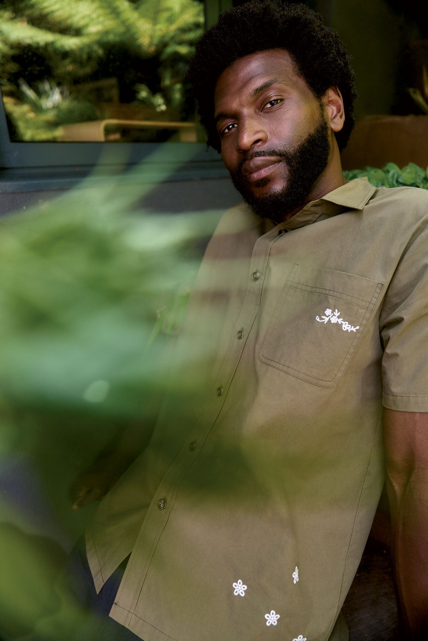 LOYLE Organic Cotton Shirt - Olive worn by a man surrounded by greenery in a relaxed setting.