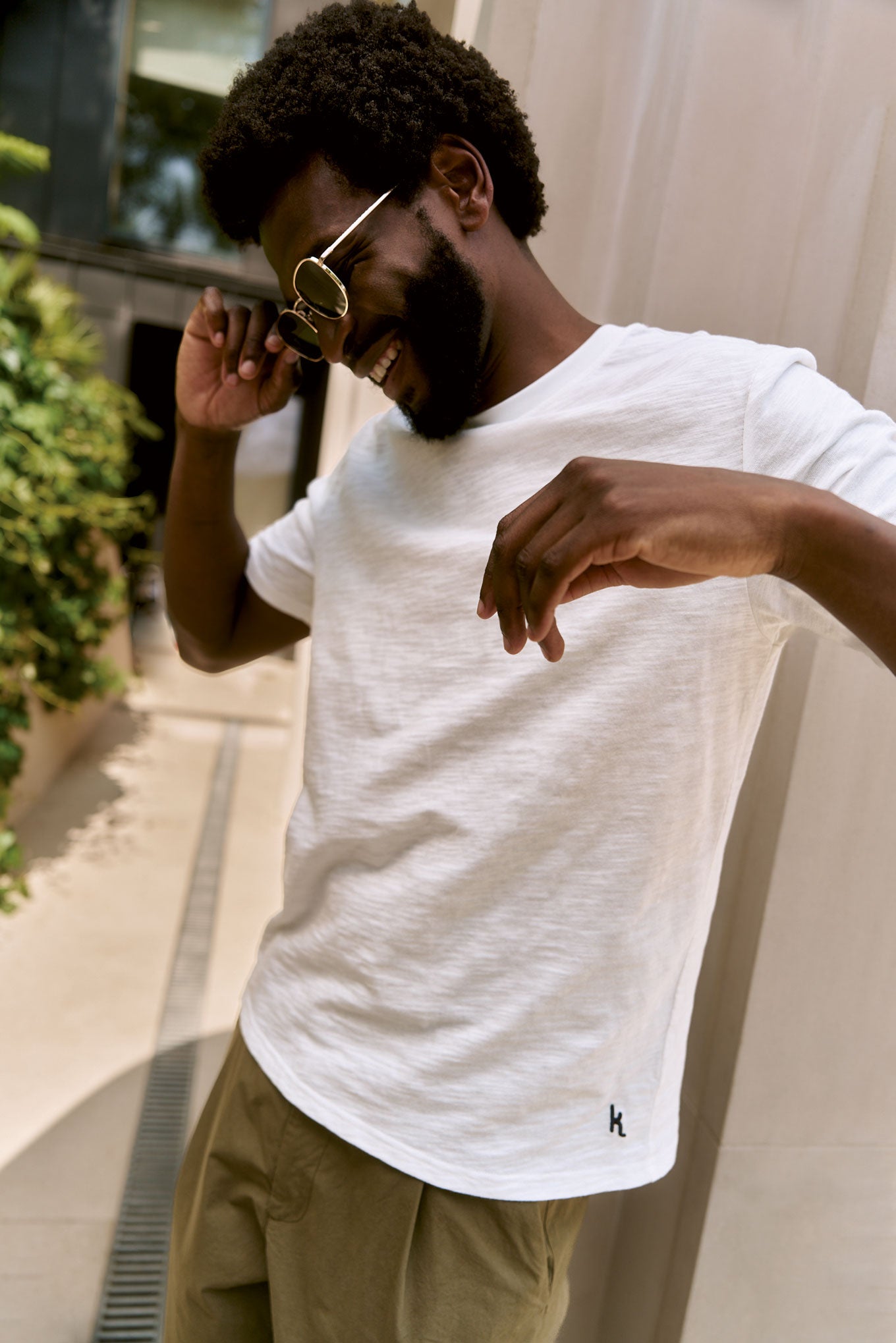 Man wearing KIN Organic Cotton Tee - White, smiling outdoors with sunglasses on.