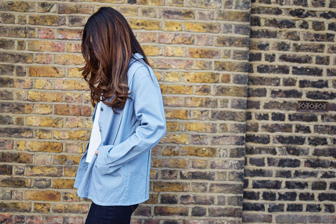 Model wearing CHORE Organic Cotton Jacket - Blue against a textured brick wall.